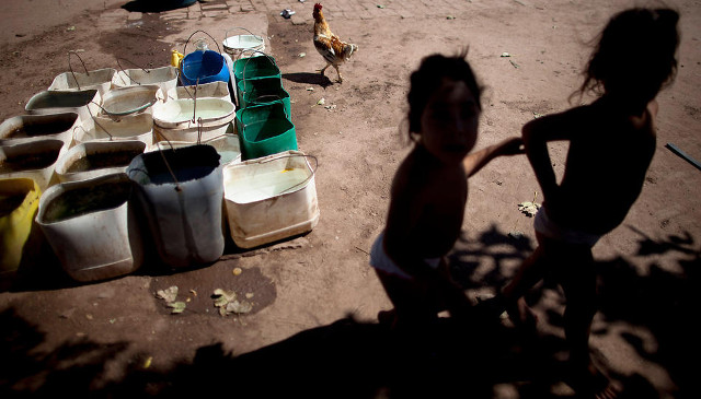 Erika, left, and her twin sister Macarena, who suffer from chronic respiratory illness, play in their backyard near recycled agrochemical containers filled with water that is used for flushing their toilet, feeding their chickens and washing their clothes, near the town of Avia Terai, in Chaco province, Argentina, on March 31, 2013. CREDIT: Natacha Pisarenko/AP
